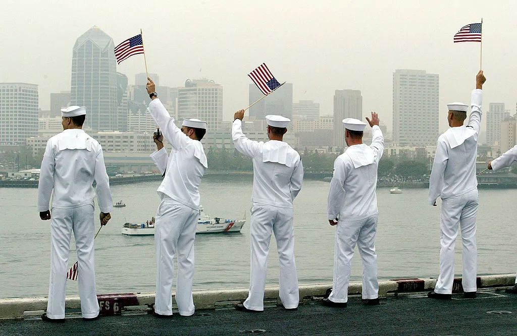 U.S. sailors wave to a passing boat while 