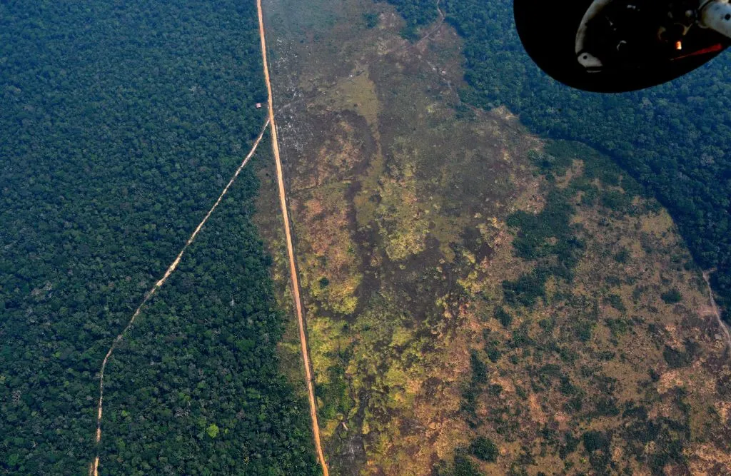 A helicopter shot reveals a large mass of land that has been deforested amongst the lush rainforest.