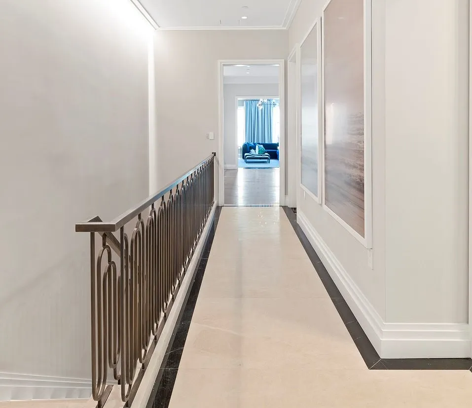 A spacious hallway with large canvas paintings on its wall across a stair railing leads into a large room.