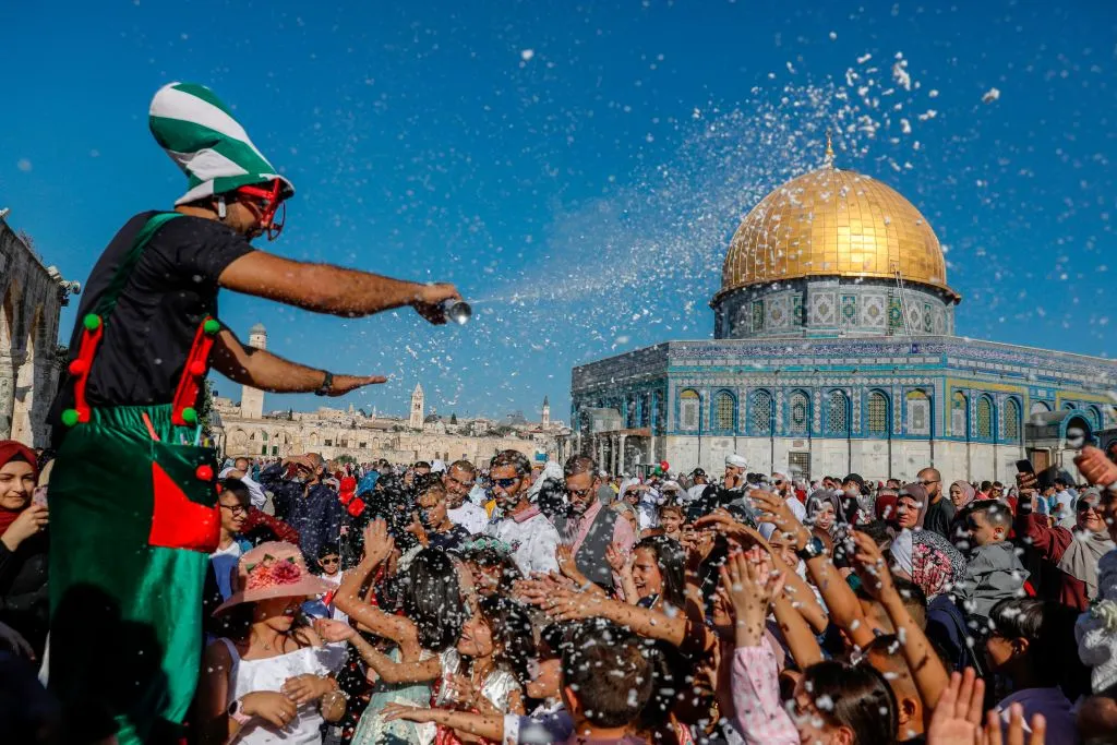 A crowd is gathered infront of the Dome of Rock mosque where they're entertained by a clown