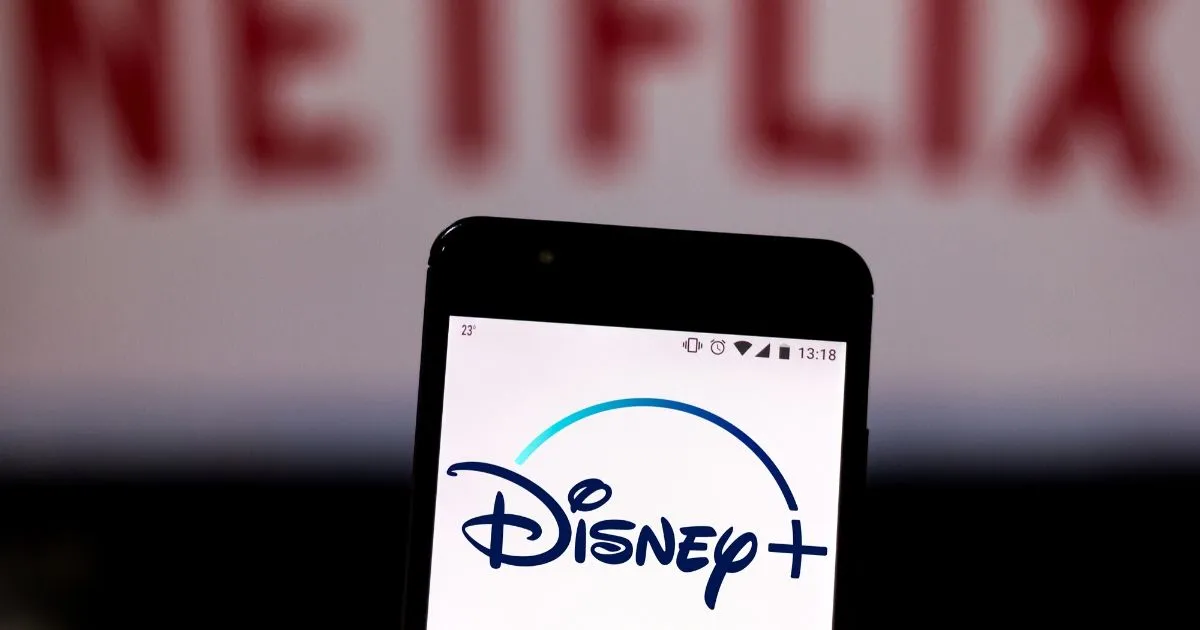 the Disney Plus logo is seen displayed on a smartphone and logo Netflix on the blurred background.